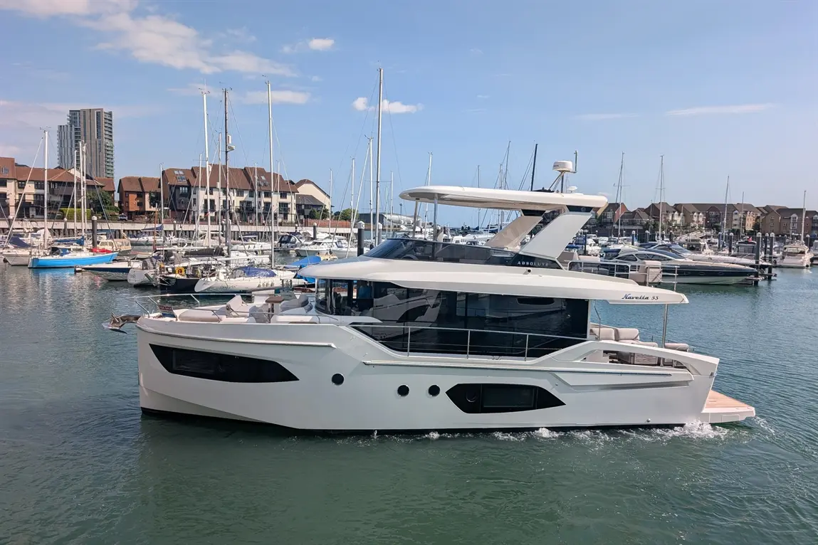 A sleek white luxury yacht named "Navetta 53" docked in a marina surrounded by various boats and buildings.